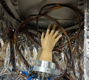 A plastic mannequin hand in a box surrounded by wires, metal, and what looks like aluminum foil.
