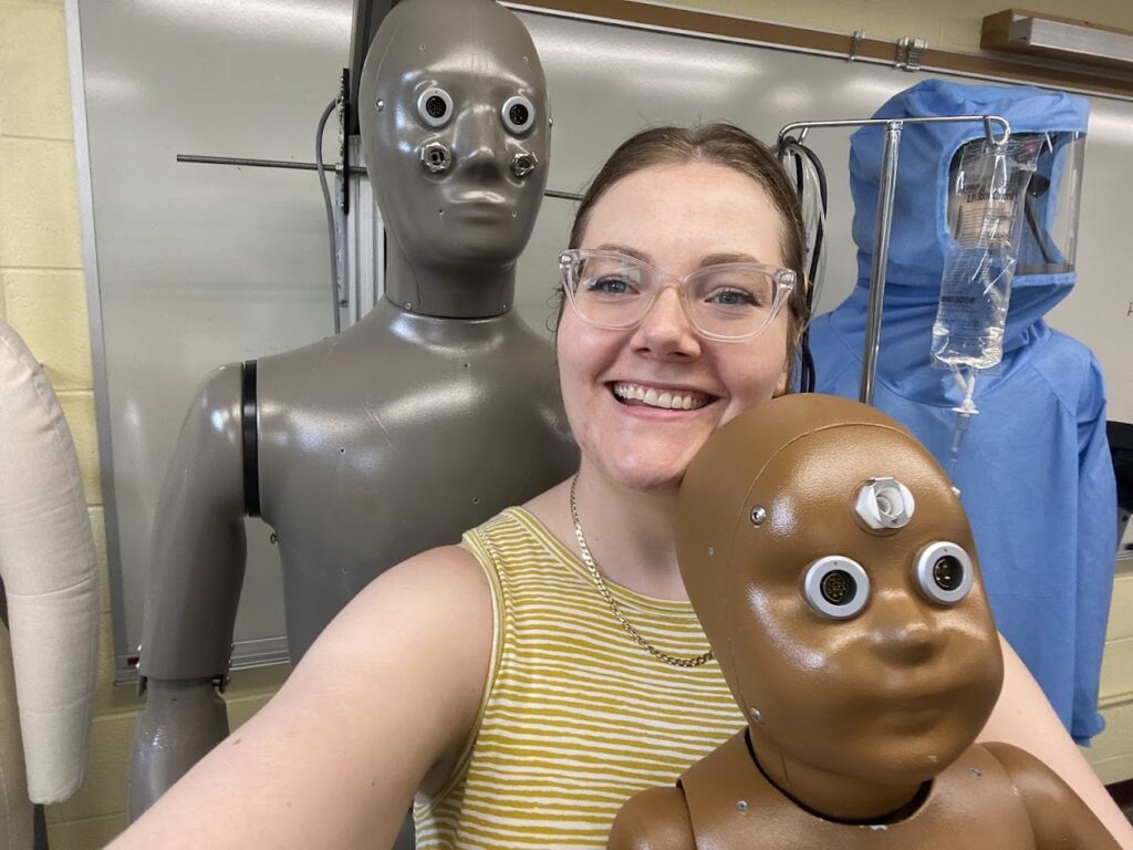 A picture of Lauren Agnew, Laboratory Coordinator and Instructor of Fashion, Interior Design & Merchandising posing with a Thermetrics-made baby thermal manikin, affectionately named Lumi and an adult thermal manikin, dubbed Norman.